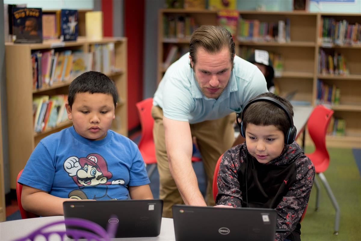 Teacher with two students looking at their laptops 