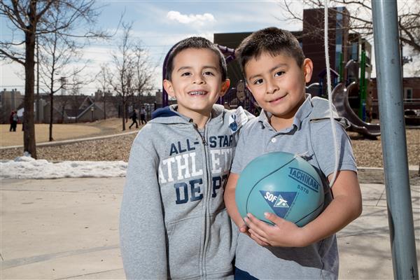 Two smiling elementary students stand on the basketball court, one holds a basketball 