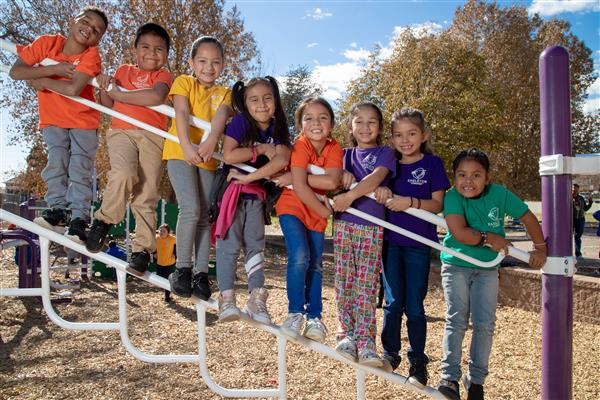 Eight elementary students lined up in a row on playground equipment 