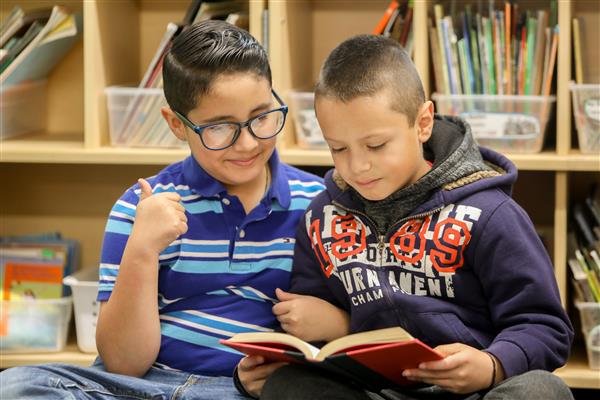 Two elementary aged students sit reading a library book 
