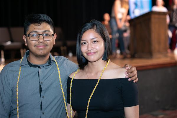 Two students stand in front of a stage with their gold Seal of Biliteracy tassels around their necks 