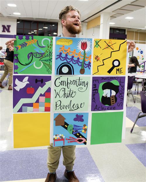 White man with beard holding up a quilt 