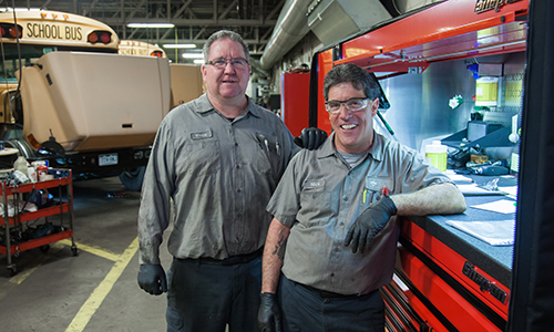 Two mechanics posing for a photo by a tool box 